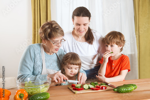 Happy family mother  grandma and two little kids are preparing the vegetables in salad in the kitchen. Healthy Lifestyle food.
