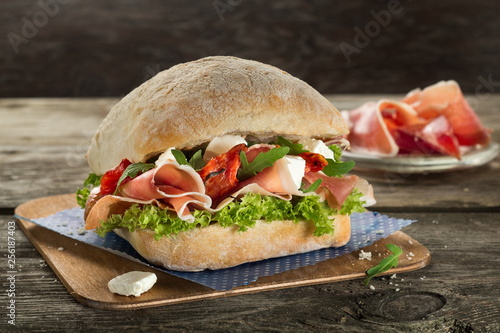 Ciabatta burger with proccuitto and salad close up on the wooden background