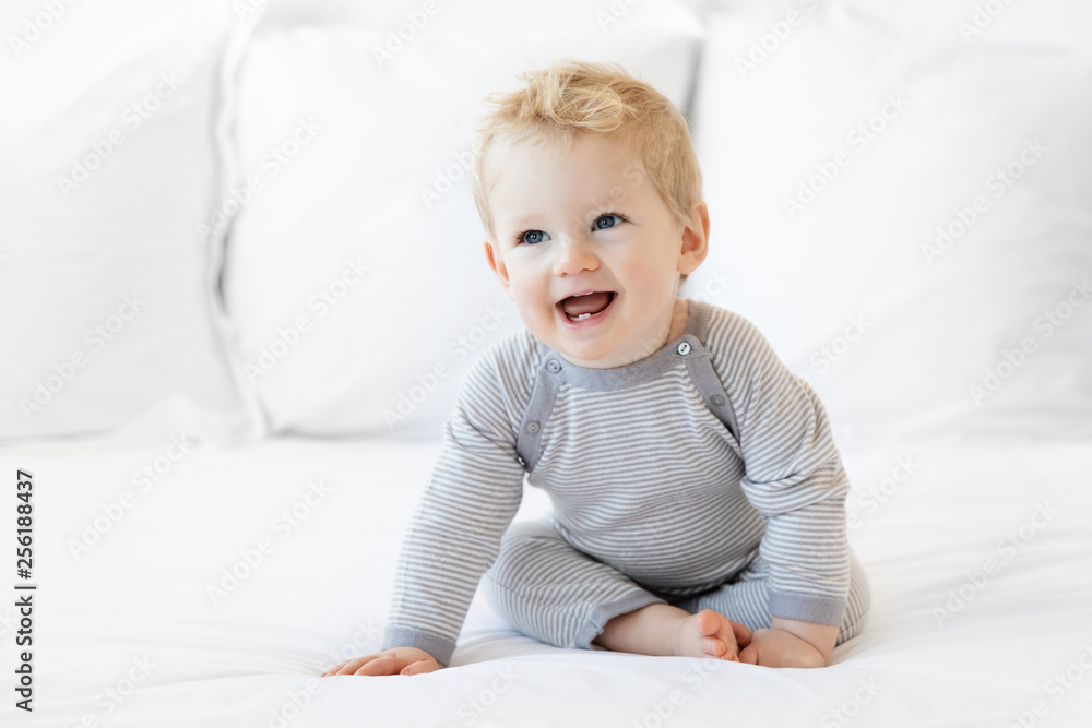 Smiling blonde baby boy sitting on white bed Smiling blonde baby boy sitting on white bed