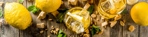 Lemonade or iced summer tea, with fresh lemon slices, sugar and mint leaf, rustic wooden table, copy space banner