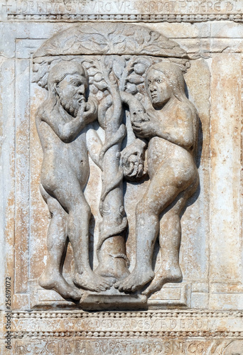 Adam and Eve eat the fruit of the forbidden tree, medieval relief on the facade of Basilica of San Zeno in Verona, Italy