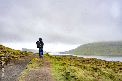 Young man walking or trekking on rural road beside the lake with bad weather raining in Faroe Islands  north Atlantic ocean  Europe