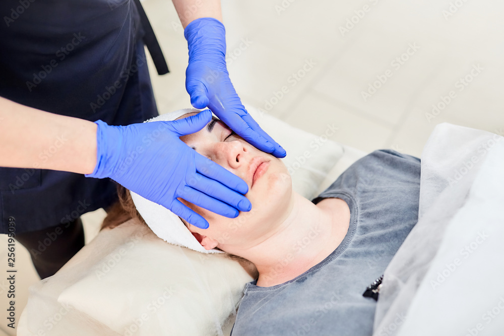 Facial massage. Hands of beautician in blue gloves. Face skin care. Woman at beauty salon. Cosmetology Facial massage. Hands of beautician in blue gloves. Face skin care. Woman at beauty salon. Cosmetology