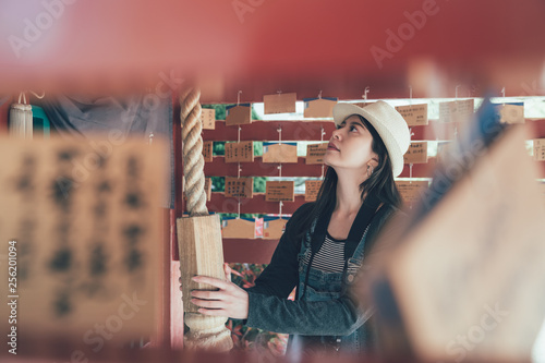 side view from wooden shrine of japanese woman pulling hand touching shimenawa rope make suzu bell at historic wooden temple. girl with hat carrying camera praying in shitennoji shinto osaka japan photo