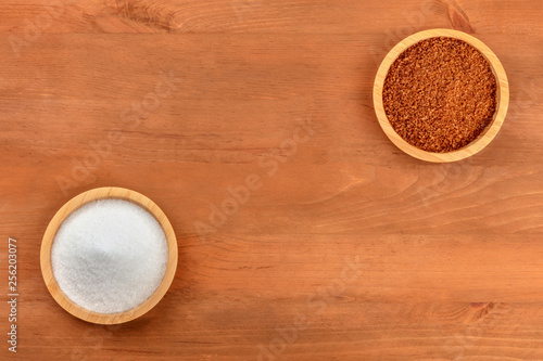 Two bowls of white and brown cane sugar, shot from above on a dark rustic wooden background with copy space