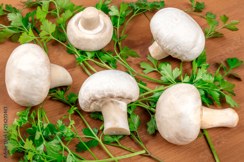 A photo of champignon mushrooms on a rustic wooden background with fresh parsley leaves