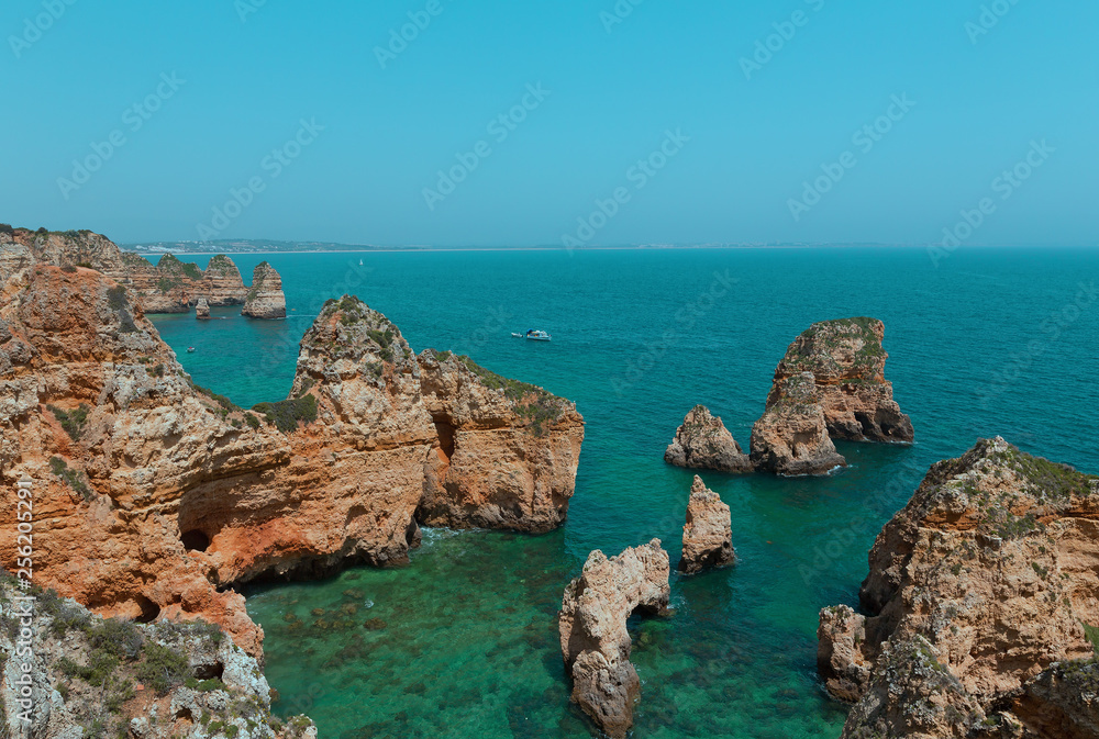 Rocky cliffs and grottoes along coastline in Algarve, Portugal. Motorboat and kayaks in turquoise sea waters on a warm spring morning.