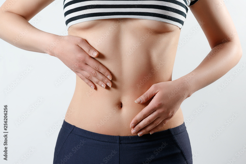 the concept of proper nutrition, women's health. close-up photo of a slender beautiful belly and navel of a woman. She touches the two palms of her hands to her waist. On white background