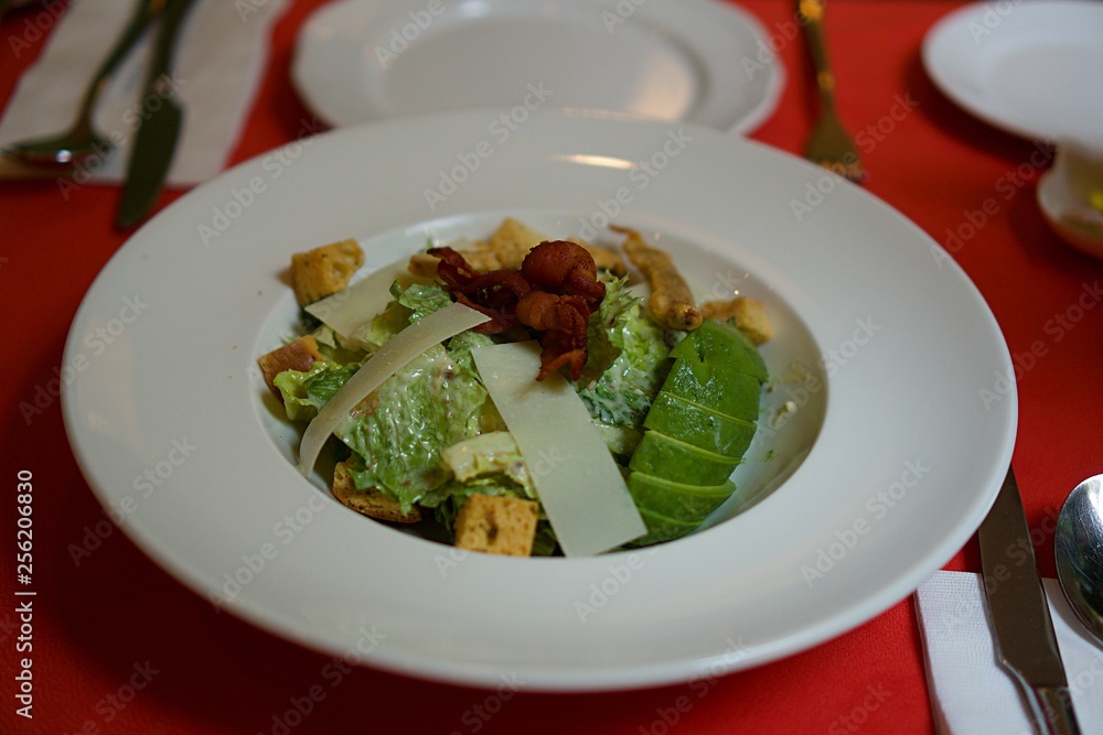 Home made caesar salad with avocado and cheese in white plate on red table. Home made caesar salad with avocado and cheese in white plate on red table.