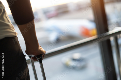 Travel tourist standing with luggage watching sunset at airport window.