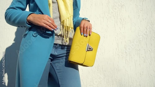 woman posing in a coat on the background of the wall with the handbag