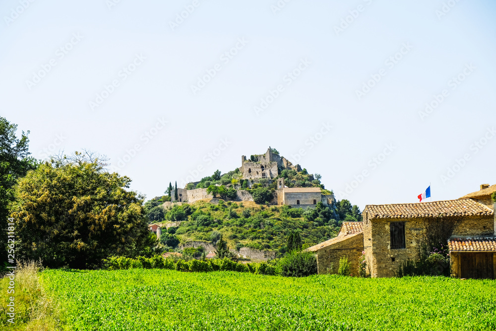 Feudal castle on the hill in the village of Entrechaux in Provence on the background of a cornfield and old buildings with a French flag.