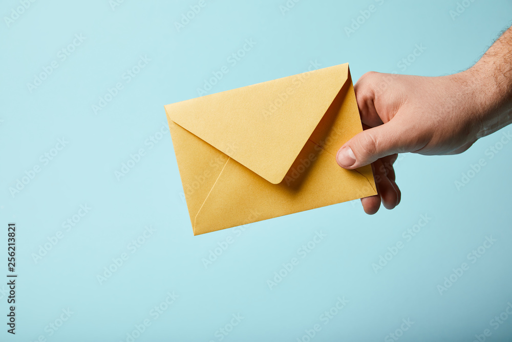 cropped view of man holding bright and yellow envelope on blue background