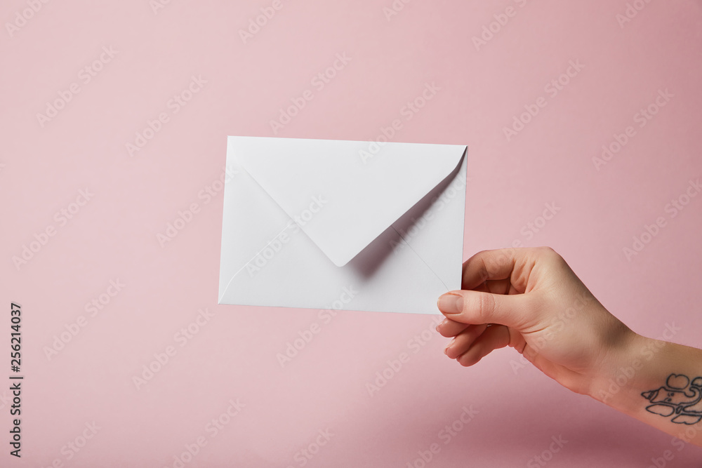 Fototapeta premium partial view of woman with tattoo holding white envelope on pink background