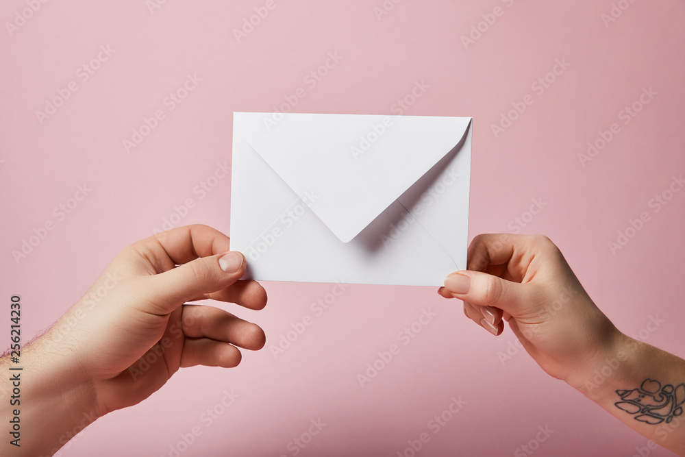 partial view of woman with tattoo and man holding white envelope on pink background partial view of woman with tattoo and man holding white envelope on pink background