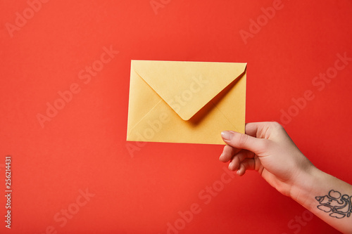 partial view of woman with tattoo holding yellow envelope on red background