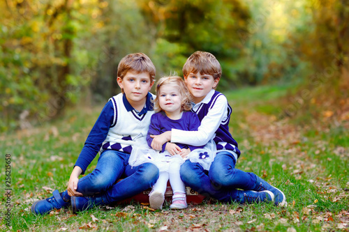 Portrait of three siblings children. Two kids brothers boys and little cute toddler sister girl having fun together in autumn forest. Happy healthy family playing, walking, active leisure on nature © Irina Schmidt