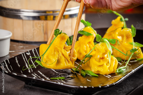 Pan-Asian cuisine concept. Wontons of yellow dough, minced meat. Japanese dumplings with minced meat. Serving dishes in the restaurant on a black plate. Background image copy space