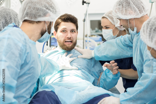 Group of surgeons holding scared male patient on surgery table