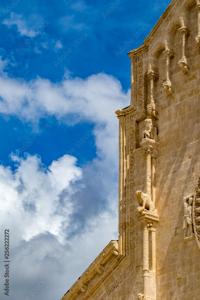 Church wall with carved stone sculpture decorations of Chiesa di Sant'Agostino, partial street view from ancient town of Matera, Basilicata, Southern Italy, cloudy summer warm August day