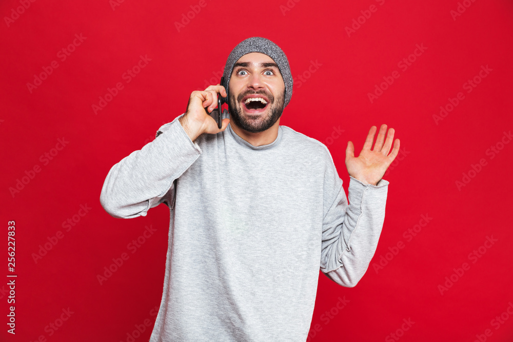 Fototapeta premium Image of successful man laughing while using cell phone isolated over red background