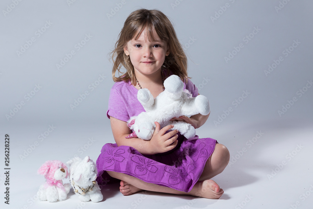 Little girl in pale purple top and purple skirt sitting holding a stuffed plush unicorn Little girl in pale purple top and purple skirt sitting holding a stuffed plush unicorn