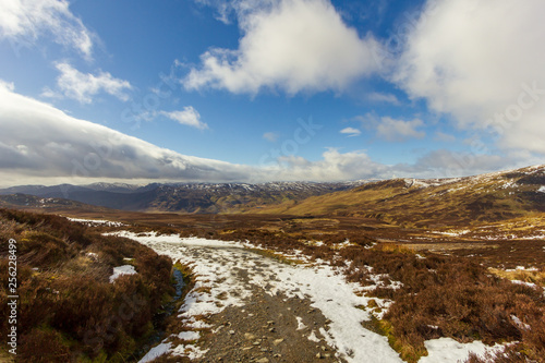 A snowy mountain path under a majestic blue sky and white clouds