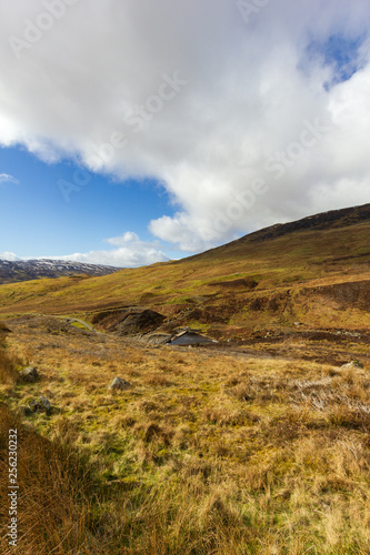 A mountain grassy slope view with a dam under a majestic blue sky and white clouds