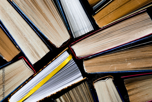 Lots of colourful thick open books stand on a dark background. ready to read
