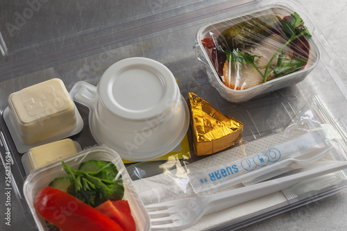 Food served on board of economy class airplane. Plastic lunchbox with food and disposable tableware.