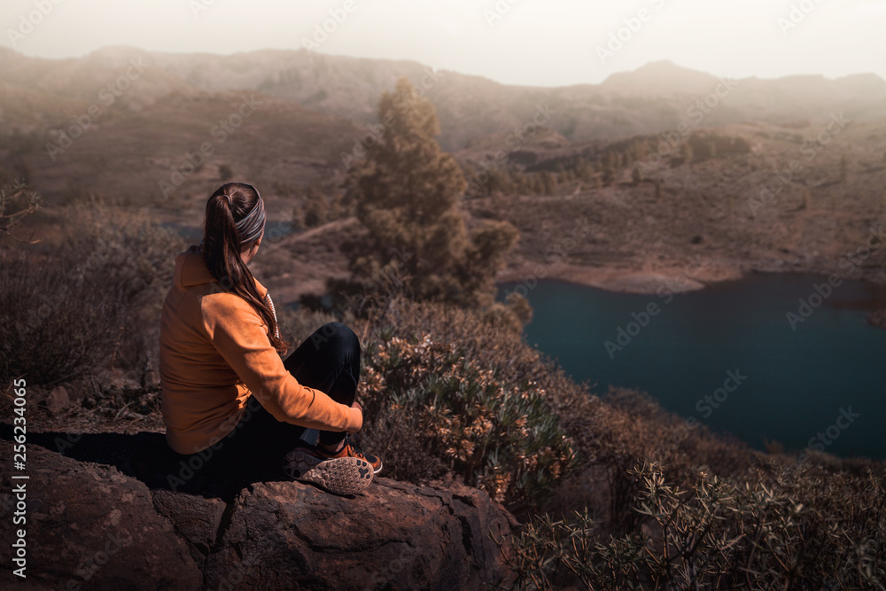 young beautiful woman sitting on rock watching the stunning landscape of gran canaria during sunset with copy space