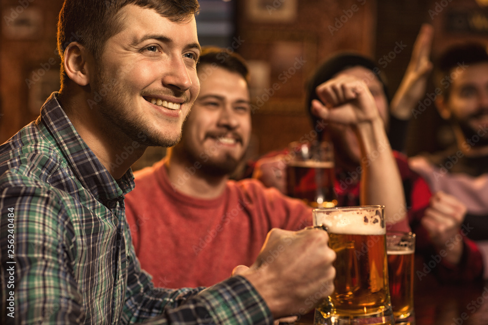 Young happy men watching football game on TV at the pub drinking beer Young happy men watching football game on TV at the pub drinking beer