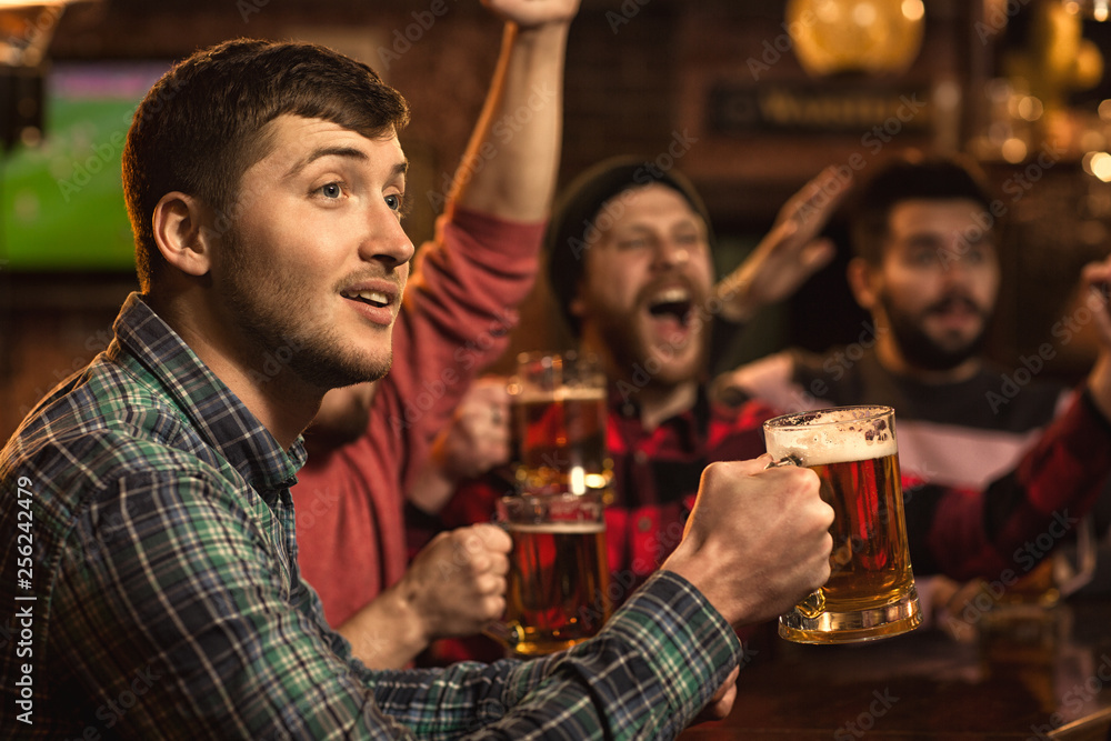 Young happy men watching football game on TV at the pub drinking beer