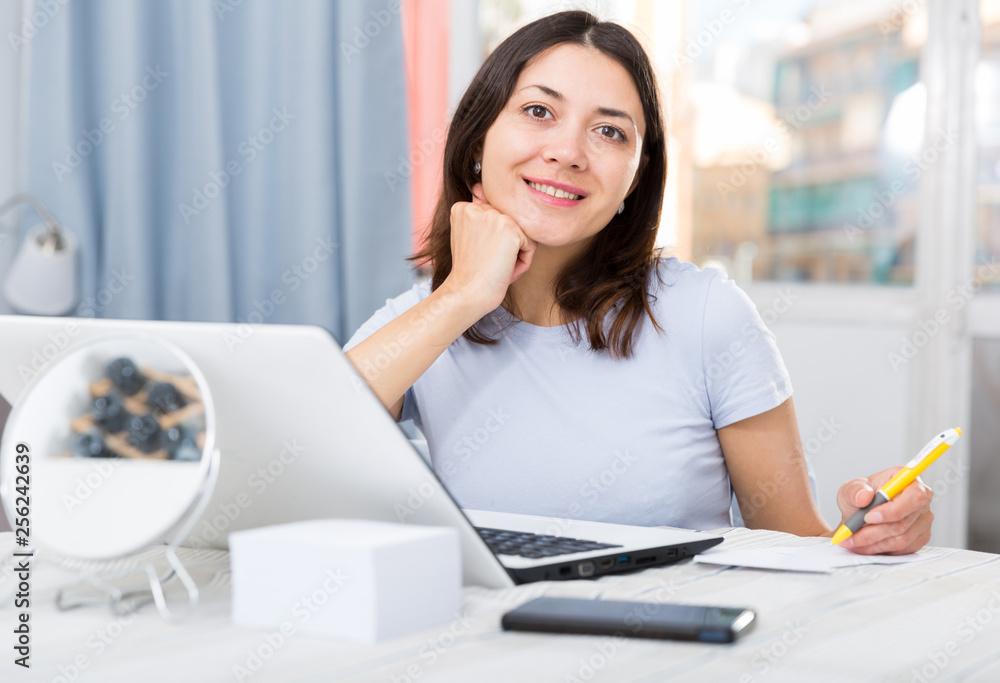 Fototapeta premium Young girl student with laptop and papers working at home