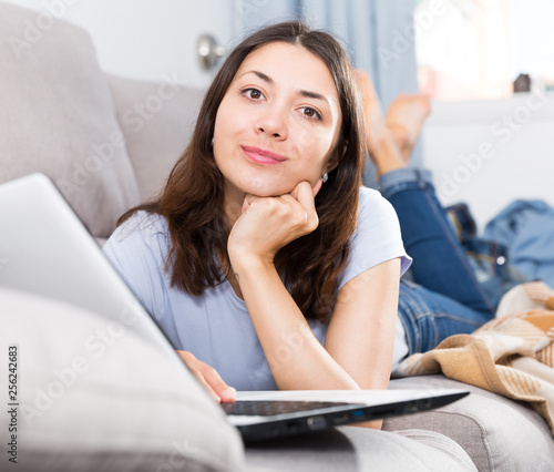 Young woman student using laptop and relaxing on sofa