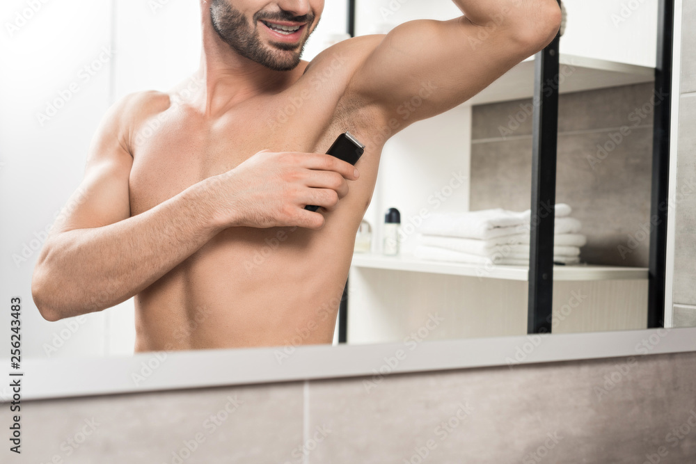 cropped view of happy shirtless man shaving armpit while standing near mirror in bathroom cropped view of happy shirtless man shaving armpit while standing near mirror in bathroom