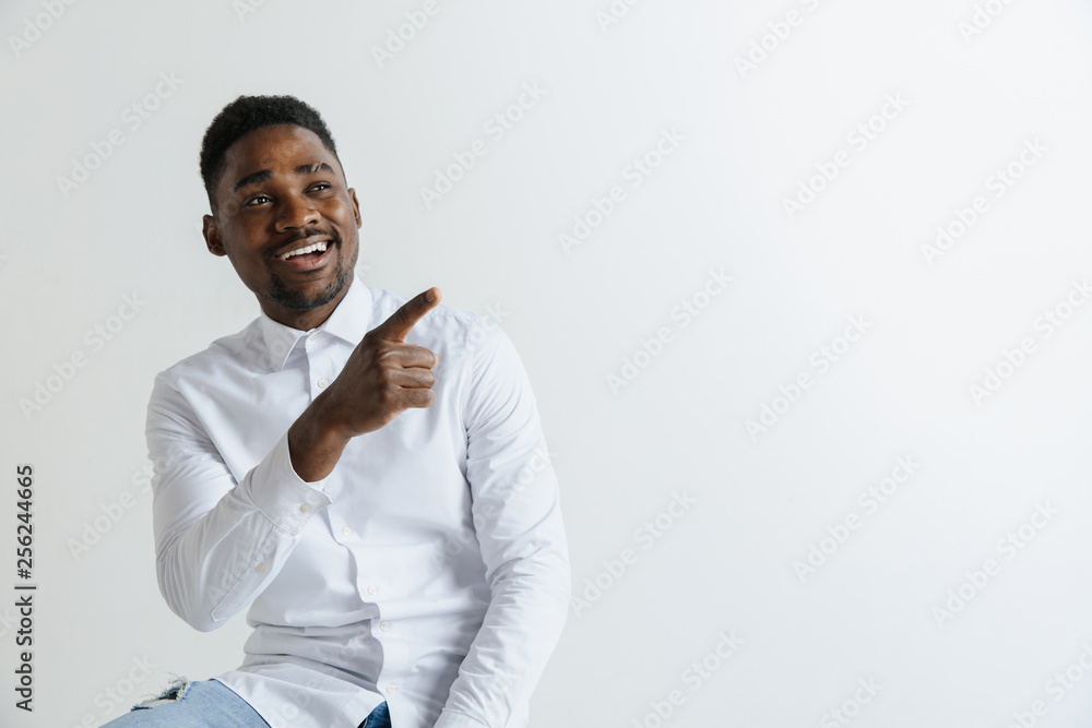 Handsome Afro American man in classic shirt is smiling, looking at camera and pointing away, against white brick wall Handsome Afro American man in classic shirt is smiling, looking at camera and pointing away, against white brick wall