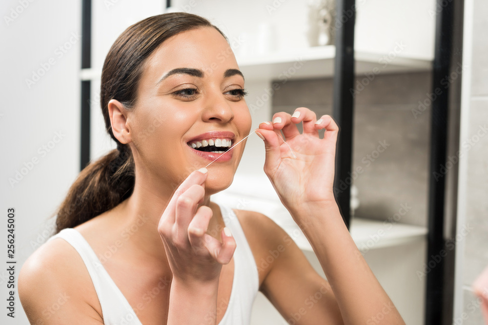 cheerful brunette woman using dental floss in bathroom cheerful brunette woman using dental floss in bathroom