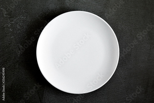 Empty white plate on black background table. Flat lay, top view, copy space