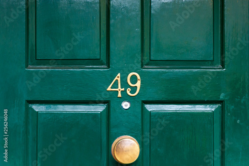 House number forty nine with the 49 in bronze on a dark green painted wooden house door with a bronze doorknocker