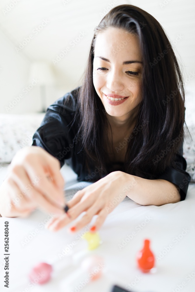 Women 30s wearing bathrobe laying in big bed and painting nails Women 30s wearing bathrobe laying in big bed and painting nails