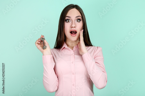 Young woman showing house keys on mint background