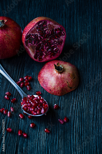 Healthy fresh pomegranates on a dark wooden background. A spoon with grains of fresh pomegranate. Vibrant focus. Dark wooden background. Side view.
