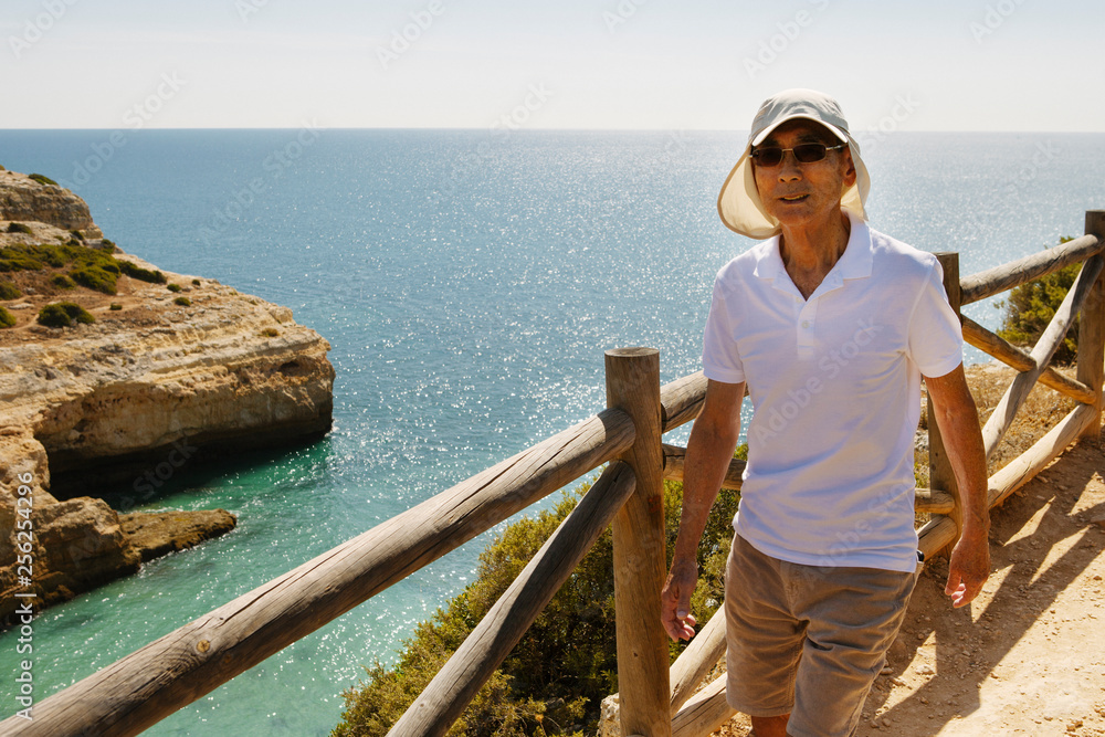 Senior man walking on cliff by railing against sea Senior man walking on cliff by railing against sea
