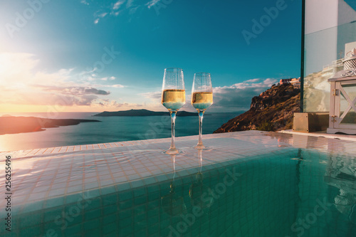 Two champagne glasses on the edge of infinity swimming pool at sunset on Santorini island