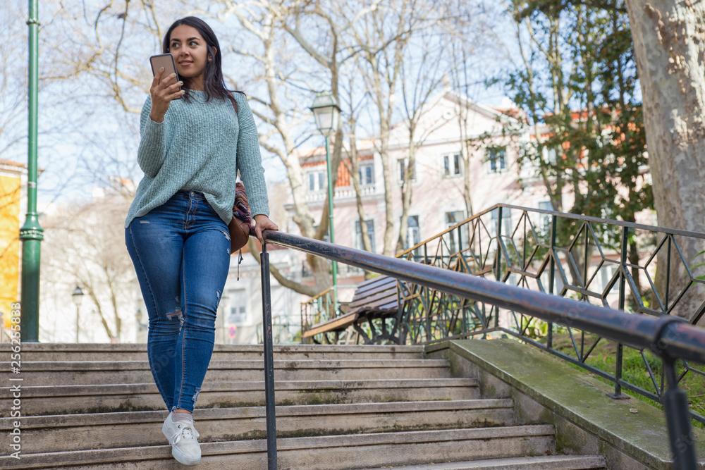 Young woman walking down city stairs and holding smartphone