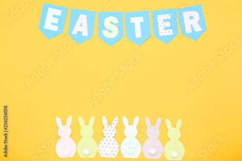 Paper rabbits with word Easter on yellow background