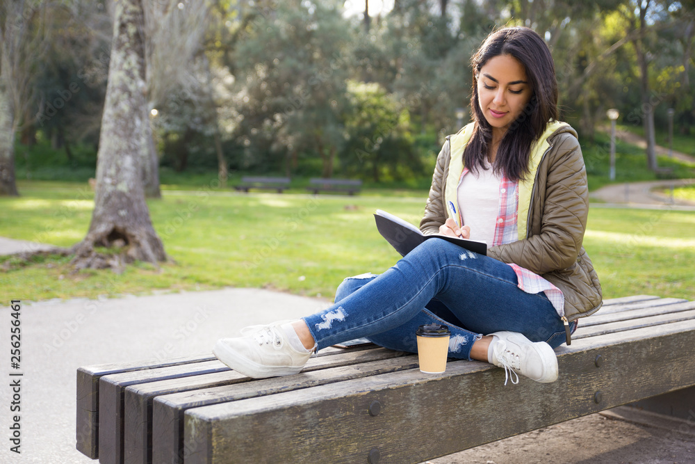 Pensive Asian girl making notes in diary while sitting in park Pensive Asian girl making notes in diary while sitting in park