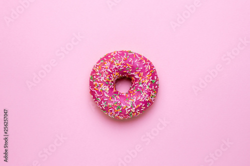 Sweet pink donut with multicolored sprinkles on a pink background flat lay