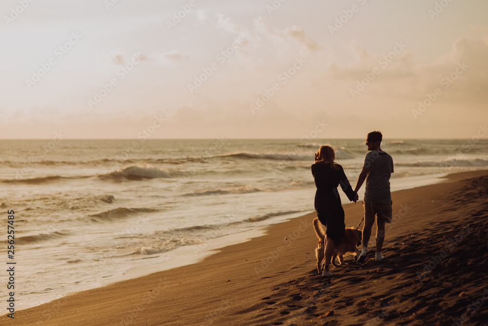 Naklejka premium beautiful happy laugh young hipster couple with golden retriever on beach. ocean an sand. waves. concepte of freedom and love.